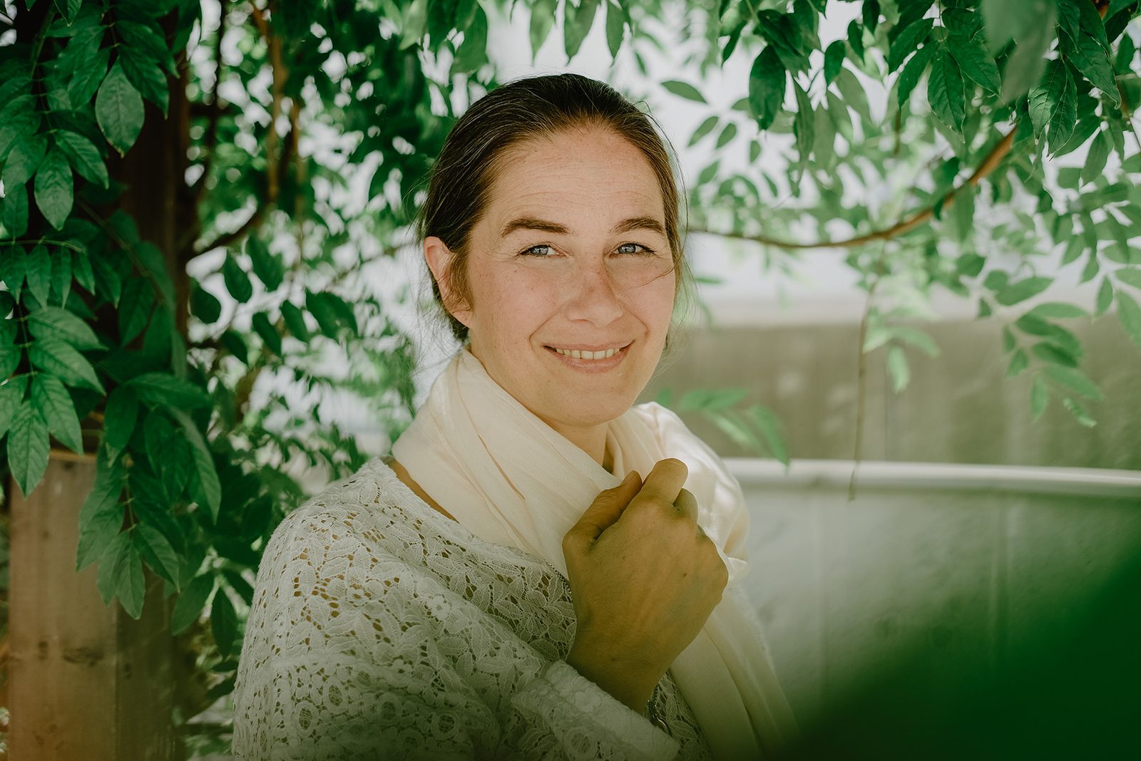 O'Shana J. Kosarev under leaves, smiling, wearing a light scarf
