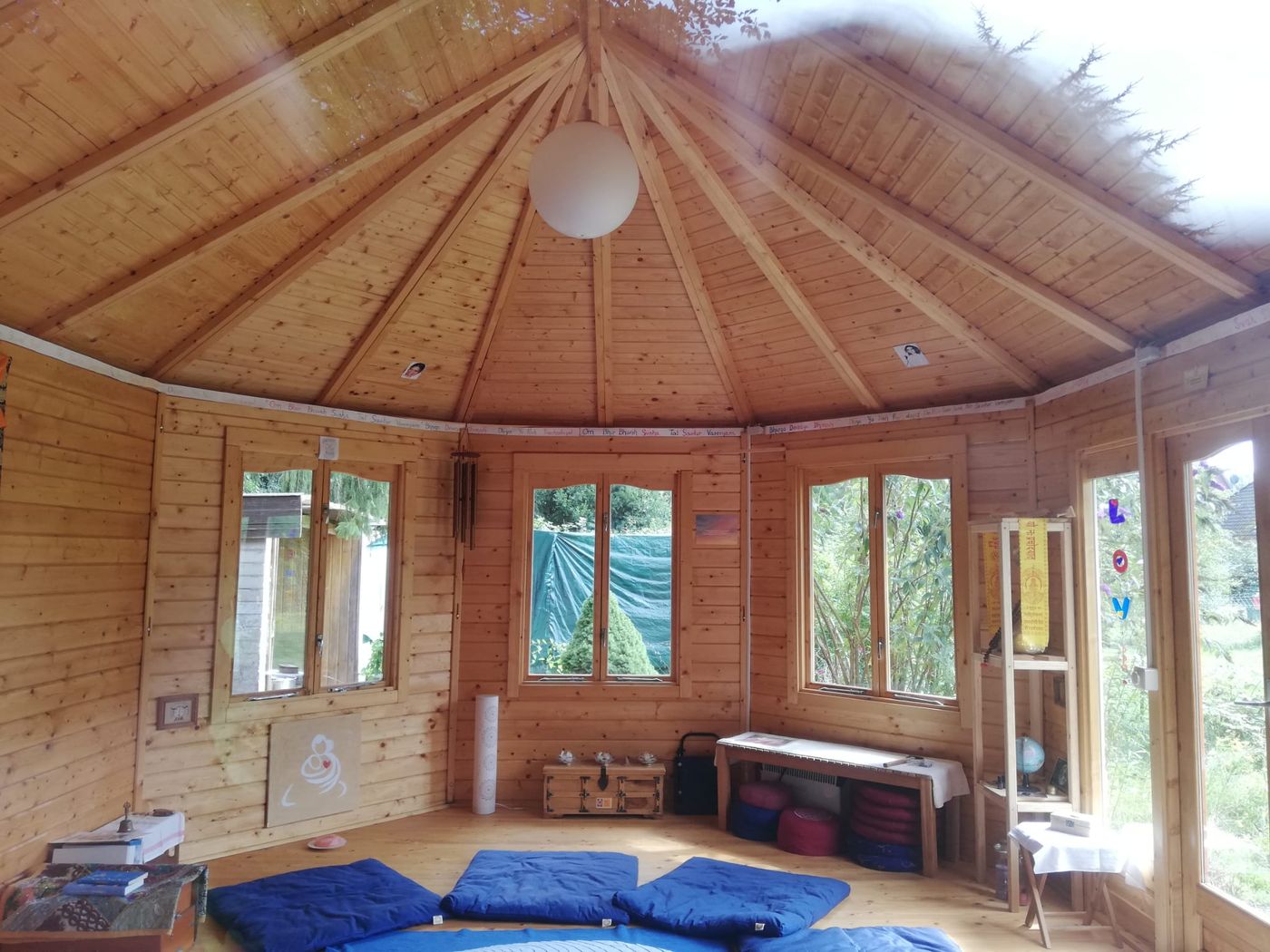 Inside an octagonal wooden pavilion, blue meditation mats on the wooden floor